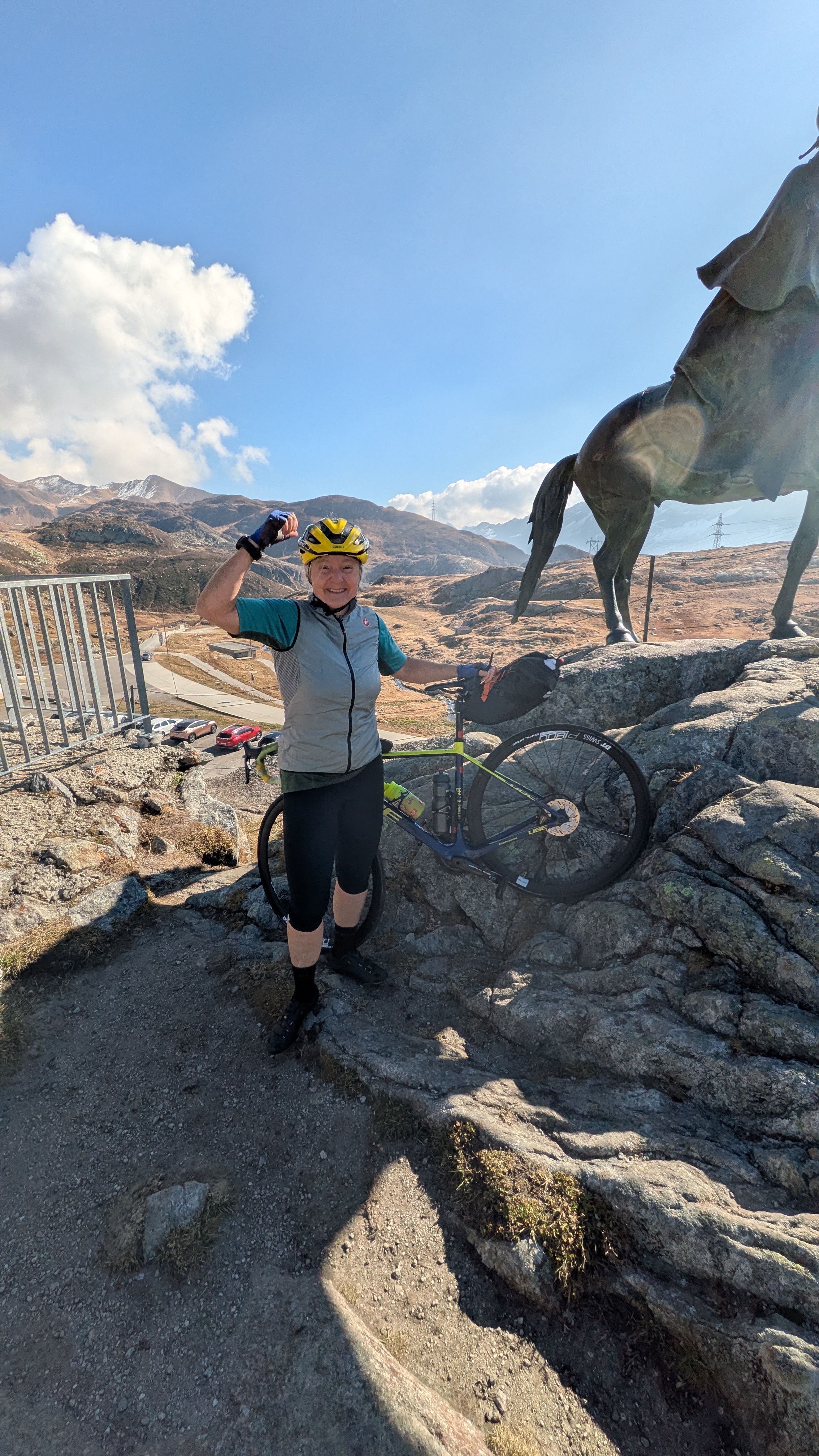 Rennradfahrerin hat ihr Rennrad zu Desaix-Statue getragen und freut sich über die erfolgreiche Passfahrt.